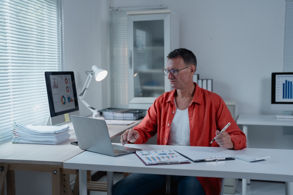 focused,mature,businessman,analyzing,financial,data,on,laptop,and,paper